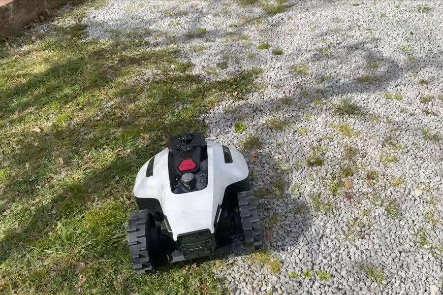 Maehroboter Vorderrad auf ebenerdig verlegtem Pflasterstein neben gruener Rasenkante